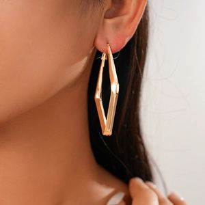 Close-up of golden geometric rhombus hoop earring on model with shiny metallic texture