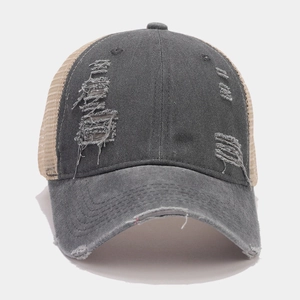 Close-up of distressed charcoal cotton and tan mesh trucker hat with torn details