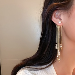 Detail of long gold tassel earrings with pearls and star charms worn by a model