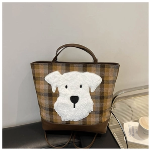 Detail of checkered plaid tote bag with plush dog patch on a leather surface
