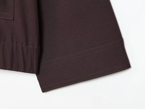 Gros plan de l'ourlet de veste marron foncé montrant la double couture et la texture