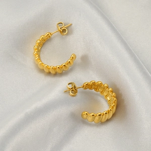 Golden C-shaped stainless steel earrings with textured finish on white silk fabric