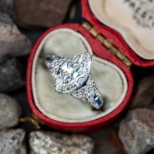 Detail of marquise-cut diamond ring with blue sapphire accents in red heart box