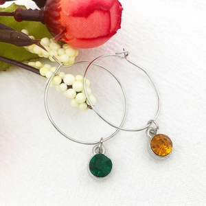 Silver hoop earrings with green and amber birthstone charms on white fabric background