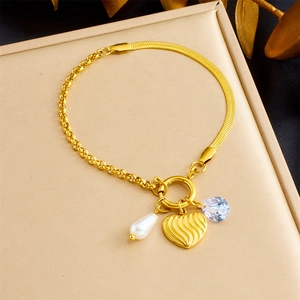 Detail of gold-plated chain bracelet with heart, pearl, and crystal charms on a metal surface