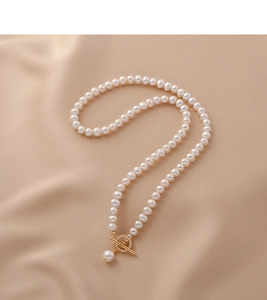 Detail of freshwater pearl necklace with gold OT buckle on beige silk fabric