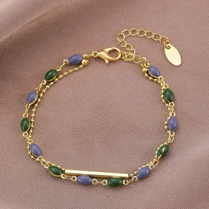 Dettaglio del bracciale a doppio strato dorato con perle ovali verdi e viola su tessuto