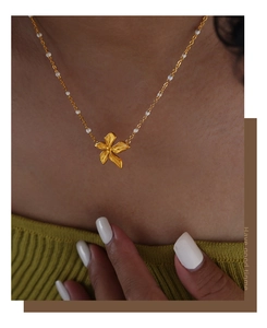 Primo piano della collana con ciondolo a fiore dorato e perline bianche sul collo di una modella