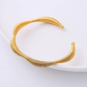 Irregular wave gold open bangle with twisted wire texture on a white ceramic plate