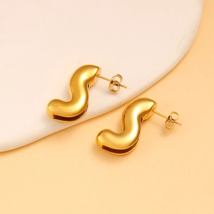 Gros plan de boucles d'oreilles dorées en forme de S sur fond de pierre blanche