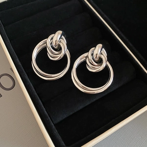 Vue macro de boucles d'oreilles créoles nouées argentées dans un écrin noir