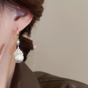 Gros plan de boucles d'oreilles dorées avec perles et zircons portées par un mannequin