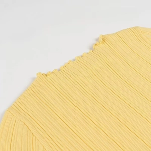 Détail du tricot côtelé jaune montrant l'ourlet ondulé et la texture verticale du tissu