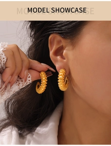 Detail view of gold-plated geometric C-shape earrings with textured beaded surface on model
