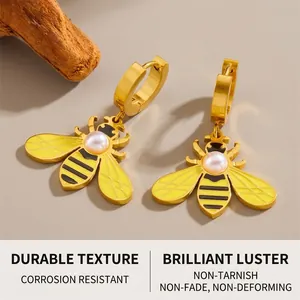 Macro shot of gold bee earrings with pearl inlay and detailed wings on a neutral base