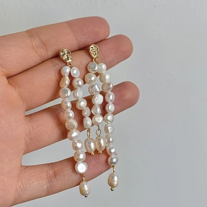 Detail of baroque freshwater pearl drop earrings with gold textured studs on hand