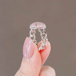 Detail of silver chain ring with pink pavé heart setting held by fingers