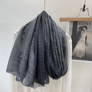 Detail of dark grey linen blend scarf showing elegant lace border on white wall