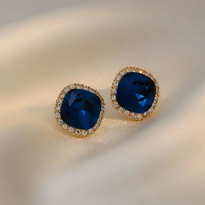 Square blue crystal stud earrings with diamond halo on beige silk fabric background