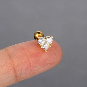 Detailed macro view of gold heart stud earring with zircons held on a fingertip