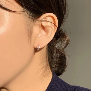 Close-up of minimalist sterling silver heart earring worn by a model in soft natural light