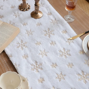 Close-up of white plush table runner with gold sequin snowflake on wooden table