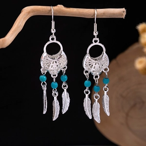 Detail view of bohemian feather tassel earrings with turquoise beads on a wooden branch