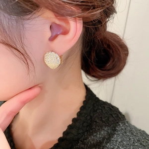 Detailed view of a gold shell-shaped earring with zircon and pearl on a model ear
