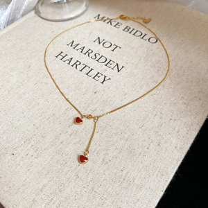 Detailed shot of golden heart pendant necklace with red enamel drops on a cream book