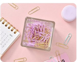 Close-up of macaron purple and gold paper clips with a clear glass storage jar