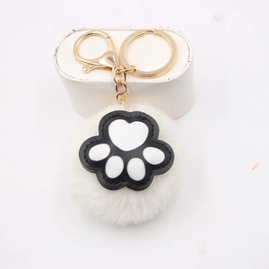Detail of white plush ball keychain with black and white cat paw charm and gold clasp