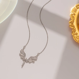 Macro shot of silver angel wing pendant with micro-pave crystals on a beige backdrop