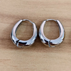 Detailed view of silver U-shaped oval hoop earrings on a textured wooden background