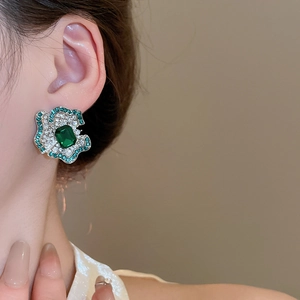 Close-up of a luxury flower earring with emerald green gem worn by a female model
