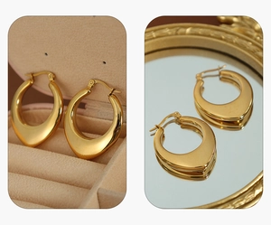 Macro detail of high-polish gold teardrop hoop earrings on a vintage mirror surface