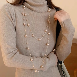 Détail d'un élégant collier de perles champagne multicouche sur un pull à col roulé brun