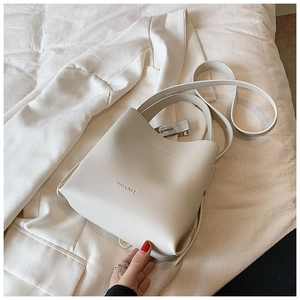 Detailed view of a creamy white leather bucket bag styled on a white blazer background