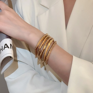 Detail of layered gold snake chain bracelet on wrist with elegant suit background