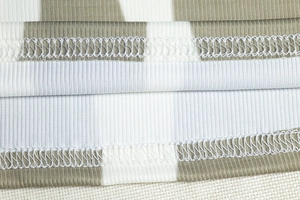 Macro view of ribbed camouflage fabric with white overlock stitching and neat hem detail