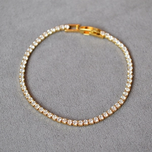Close-up of golden tennis bracelet featuring sparkling white cubic zirconia and buckle clasp