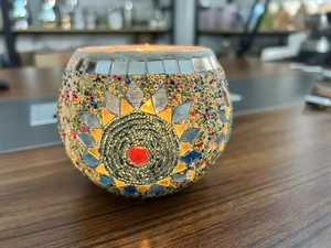 Close-up of handmade mosaic glass candle holder with sun pattern and warm candle glow