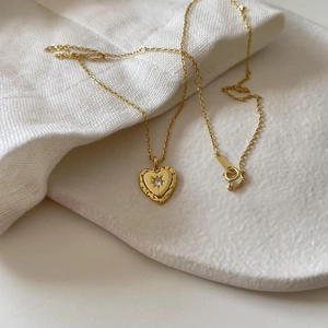 Elegant gold heart necklace with a sparkling starburst zircon on a white ceramic plate