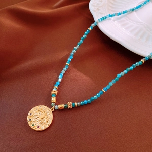 Detailed shot of blue beaded necklace with a golden evil eye pendant on brown silk fabric