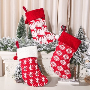Three knitted Christmas stockings with reindeer, tree, and snowflake patterns on a fireplace
