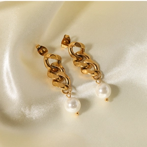Detail of gold chain earrings with white pearls resting on soft beige silk fabric