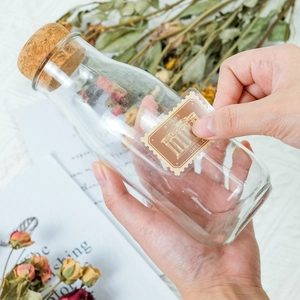 Applying vintage stamp sticker with Athens Acropolis to glass bottle with cork and petals