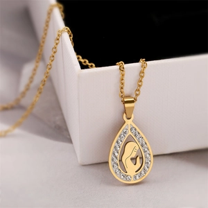 Detail of gold teardrop pendant with Virgin Mary silhouette and crystals on a white jewelry box