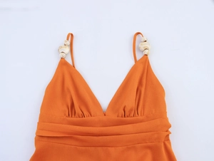 Détail d'une robe orange à col en V avec tissu texturé et perles sur les bretelles
