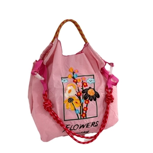 Pink nylon tote bag with floral embroidery and red woven rope handles on white background