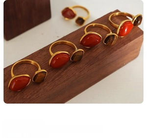 Detail view of gold-plated rings with red agate and tiger eye stone on wood base